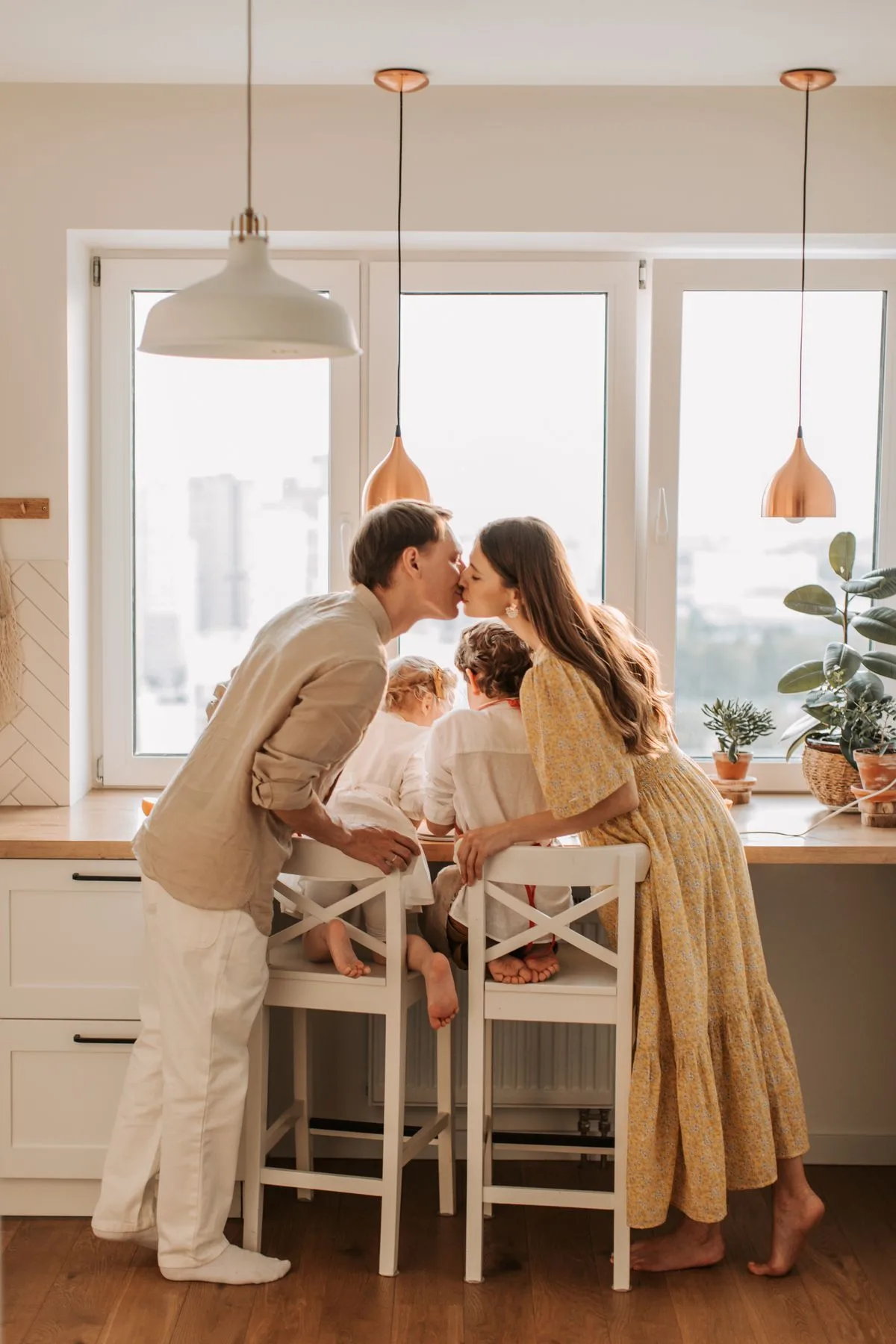 Deux parents s'embrassent au-dessus de leurs enfants dans une cuisine lumineuse